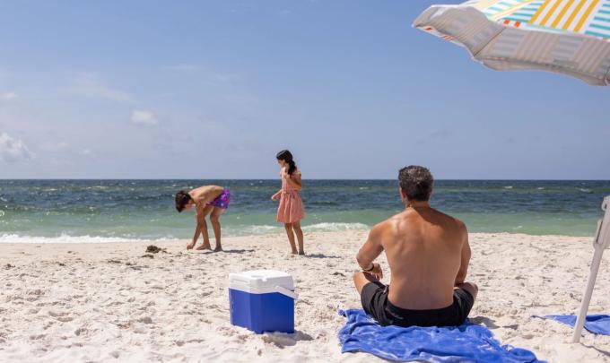 Dad sitting an umbrella on the beach watching his kids play near the shore