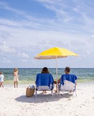 Parents sitting under a beach umbrella watching their kids walk along the shore in Gulf Shores